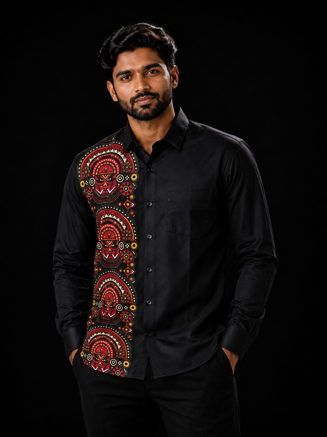 Man wearing a black full-sleeve shirt with a bold geometric Theyyam mandala art panel on the left in reds, pinks and gold dots